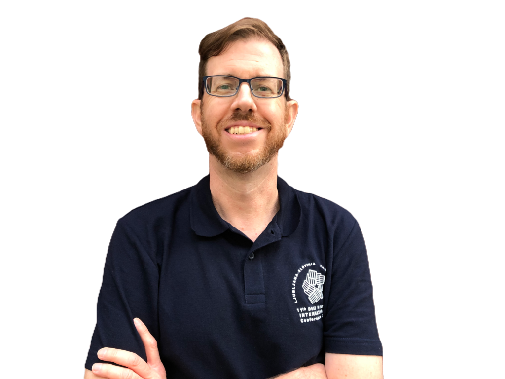 A white man with red hair and a beard, smiling with his arms folded.