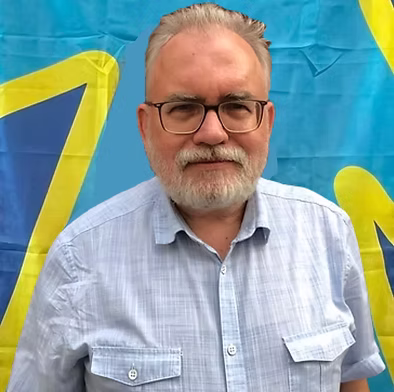 A white man with a full beard and glasses, in front of the deaf flag.